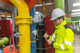 Technician in hard hat inspecting industrial pipes and valves in a brightly colored plant room