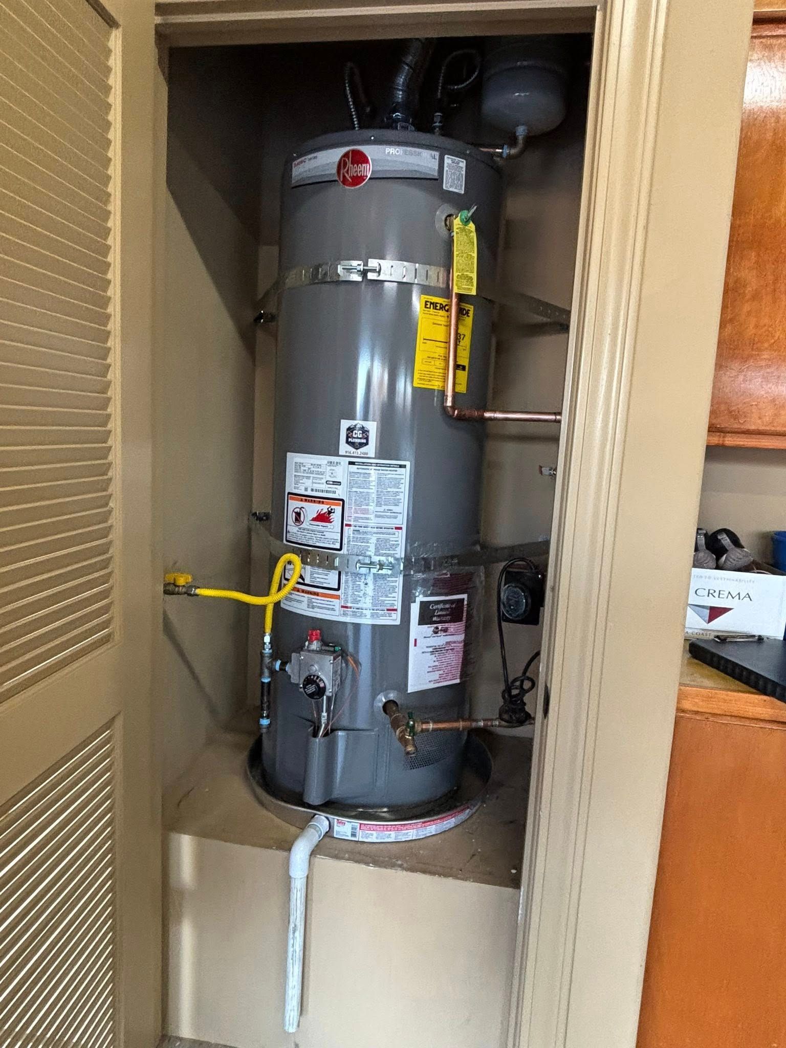 A grey Rheem water heater installed inside a small indoor utility closet.