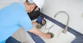Technician using a leak detector at a kitchen sink with running water