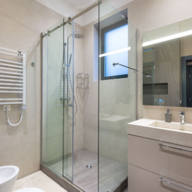 Modern bathroom with glass shower enclosure, sink vanity, window, and towel radiator