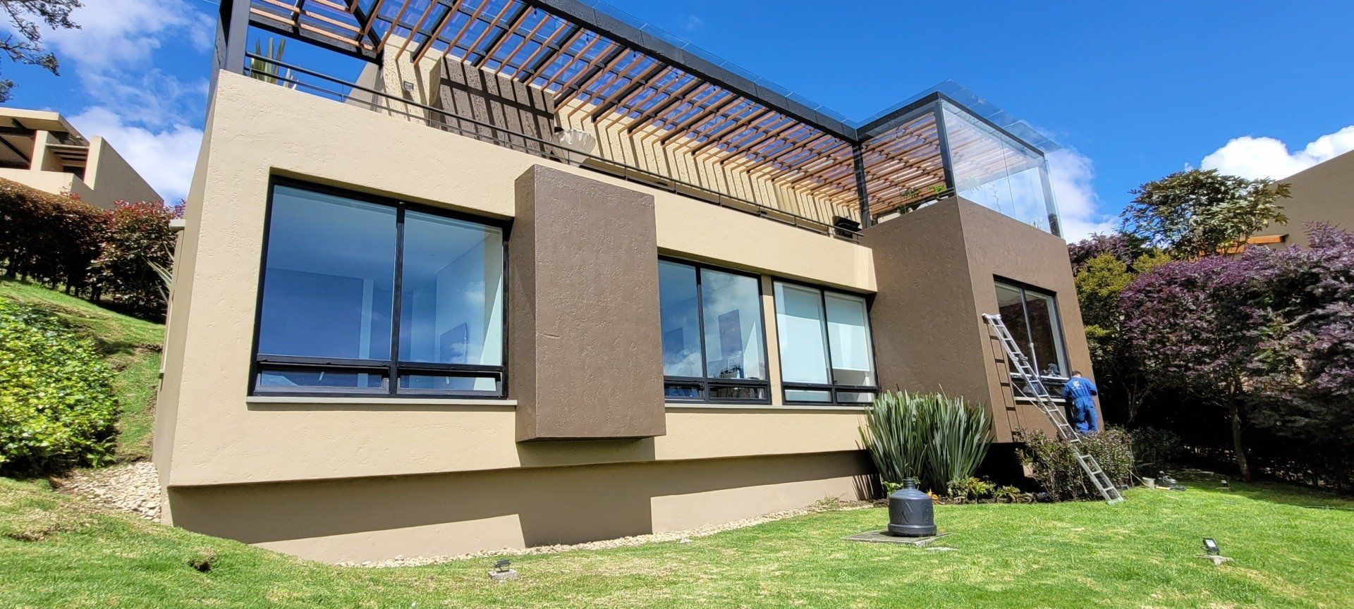 Una casa grande con muchas ventanas está situada en la cima de una exuberante ladera verde.