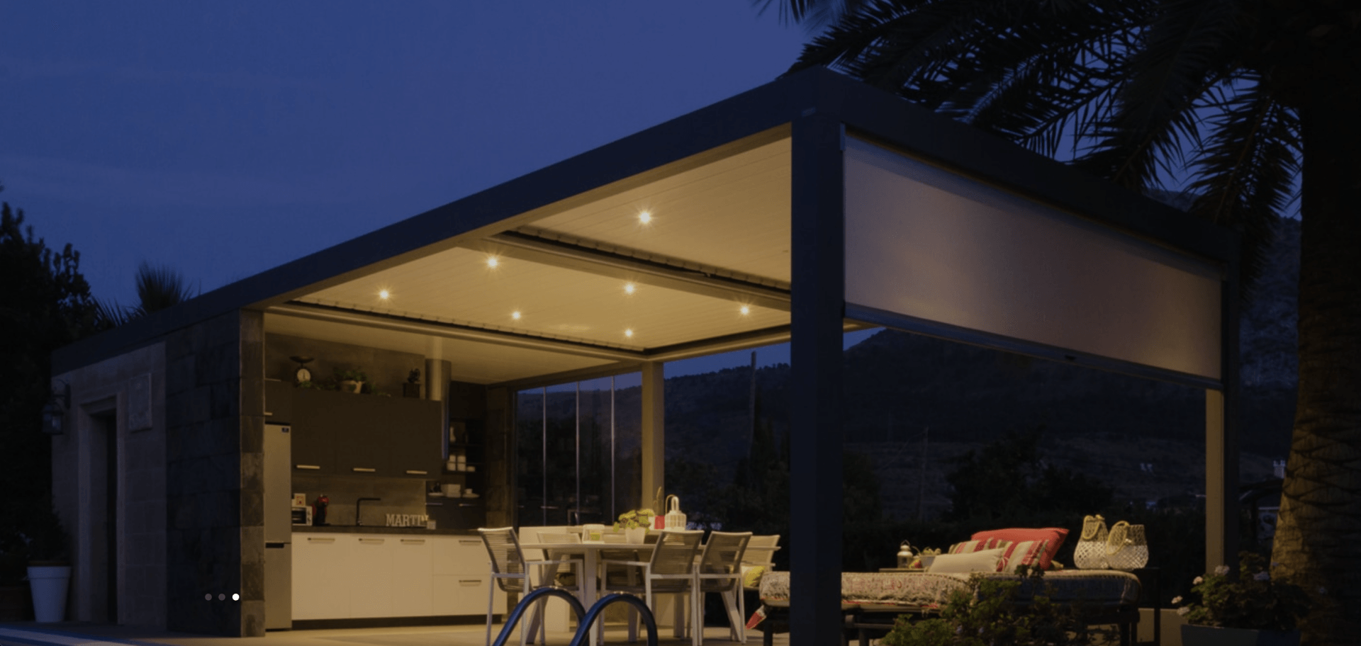 Una pérgola con una mesa y sillas debajo se ilumina por la noche.