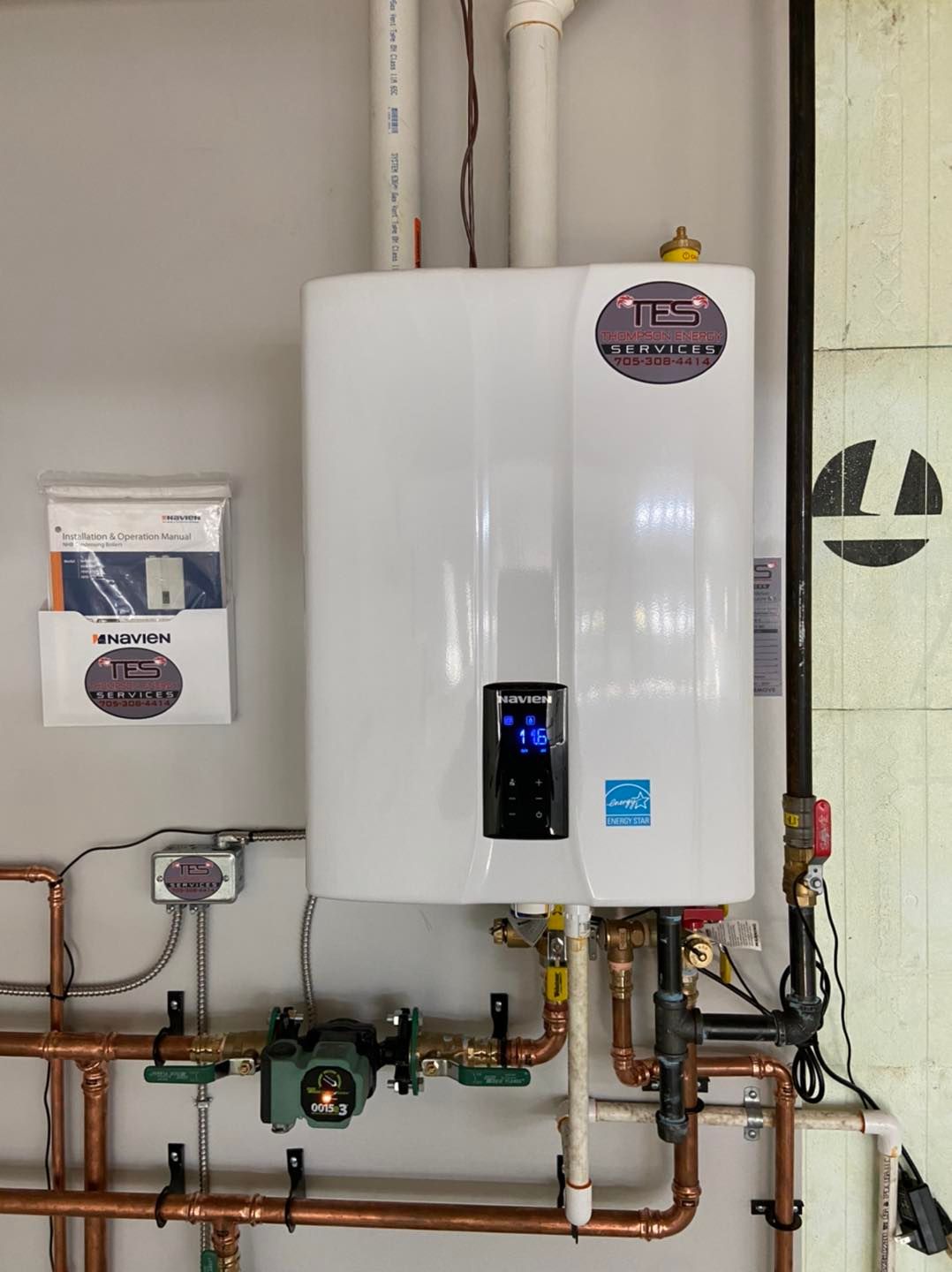 A white water heater is hanging on a wall next to copper pipes.