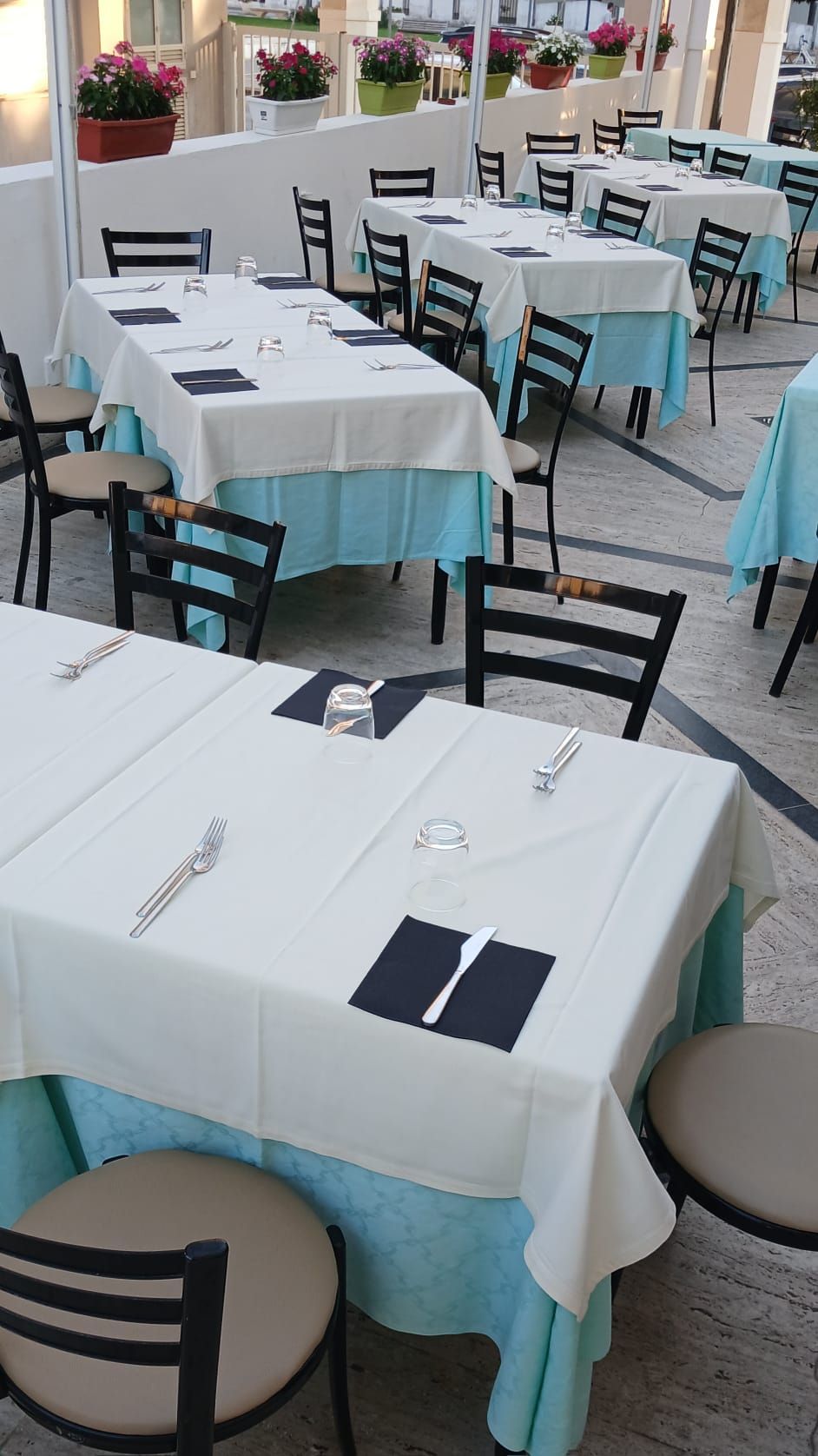 Caffè all'aperto con tovaglie bianche, dettagli turchesi e sedie nere disposte con cura.