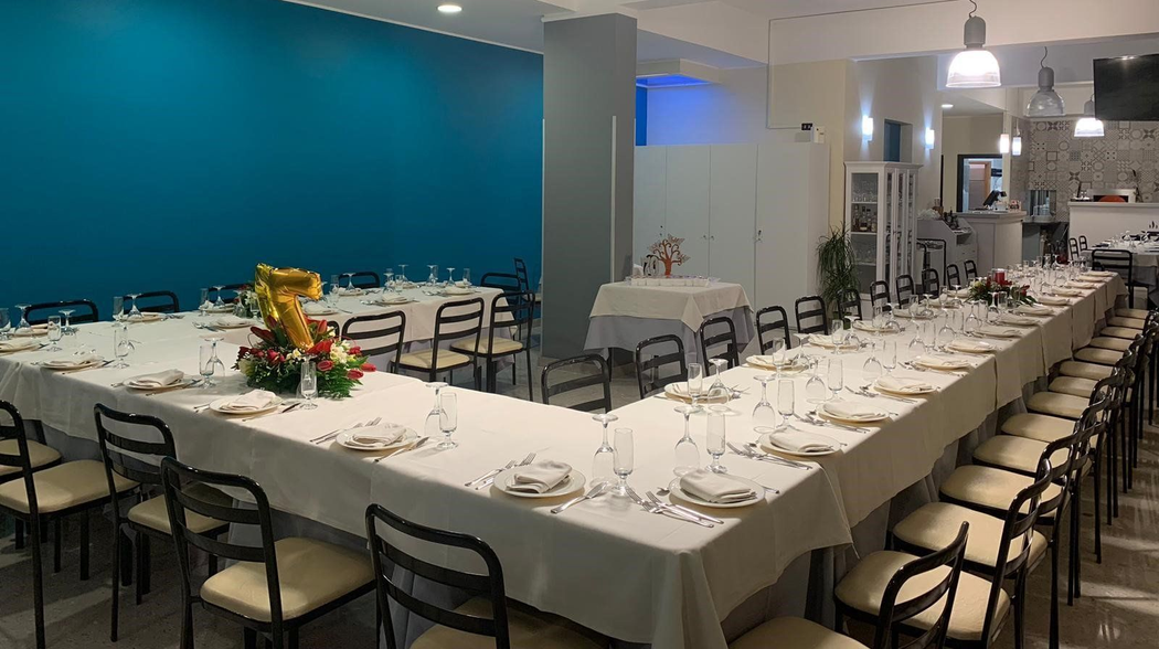 Lunghi tavoli da banchetto apparecchiati per un evento con servizio di catering in una luminosa sala da pranzo con pareti blu e grigie.