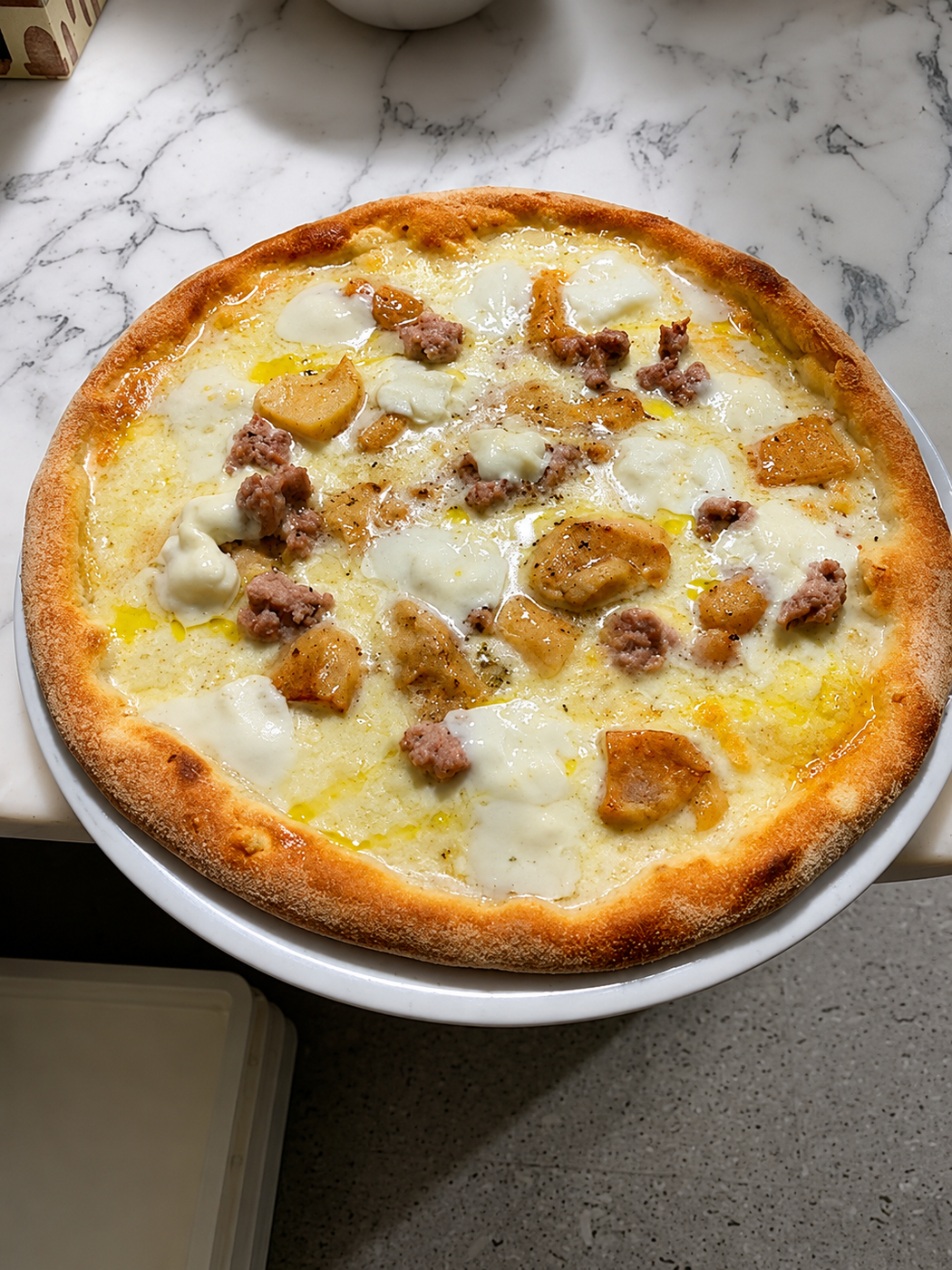 Pizza al formaggio con condimenti dorati su un piatto bianco appoggiato su un piano di marmo.