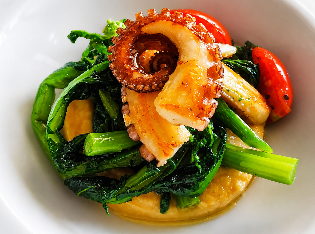 Frutti di mare misti e verdure su un piatto bianco, con polpo, verdure a foglia verde e peperoni rossi.