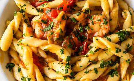 Penne condite con salsa di pomodoro, gamberi ed erbe aromatiche tritate, in una foto ravvicinata di una ciotola.