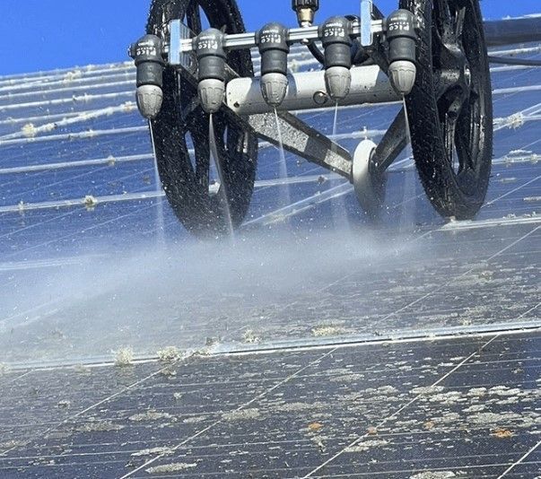 Ein Reinigungsroboter sprüht Wasser auf ein Solarpanel und entfernt so Schmutz und Ablagerungen.