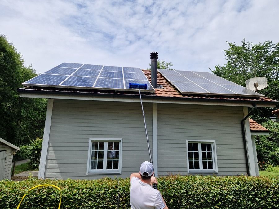 Ein Mann reinigt das Dach eines Hauses mit einer Bürste.