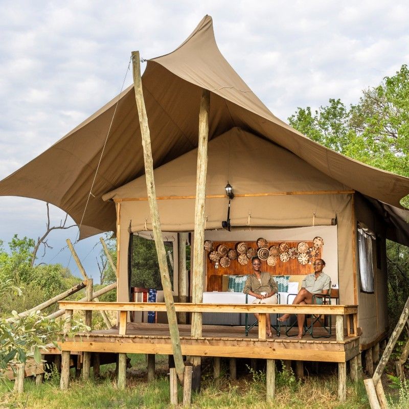 The exterior of a luxury tent at Camp Khwai in the Okavango Delta, Botswana, is captured in this inviting travel photograph, showcasing the lodge’s seamless integration with its pristine wilderness surroundings. Elevated on a wooden deck, the tent overlooks grassy floodplains and meandering waterways, offering unobstructed views of the Delta’s abundant wildlife. Natural materials and neutral tones blend harmoniously with the landscape, emphasizing comfort, elegance, and respect for the environment. Soft morning or evening light enhances the textures of the canvas, wood, and surrounding vegetation, creating a serene, immersive atmosphere. Inspiration Africa curates bespoke, tailor-made journeys to Botswana and across Africa, combining exclusive safari experiences with luxury accommodations in extraordinary natural settings.