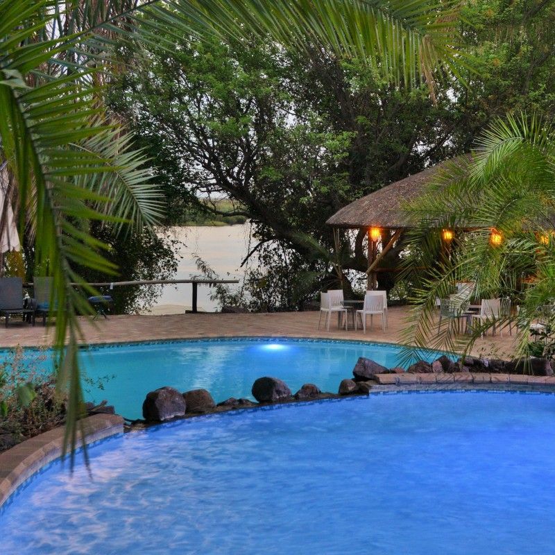 The swimming pool at Cresta Mowana Safari Resort in Botswana is featured in this serene travel photograph, set along the banks of the Chobe River and surrounded by lush riverside vegetation. The expansive pool area offers a refreshing retreat from the heat of the day, with calm waters reflecting palm trees and open skies. Sun loungers and shaded seating provide inviting spaces for relaxation, while the natural setting allows guests to enjoy views of passing wildlife and birdlife along the river’s edge. The atmosphere blends comfort and leisure with the untamed beauty of the Chobe region, creating a peaceful contrast to nearby safari adventures. This scene captures the resort’s appeal as a relaxing base for exploring one of Botswana’s most wildlife-rich destinations. Inspiration Africa specializes in bespoke, tailor-made journeys to Botswana and across Africa, crafting unforgettable travel experiences in exceptional wilderness locations.