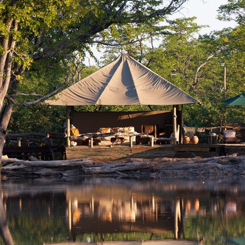 The exterior of one of the tents at Hyena Camp in Botswana is featured in this atmospheric travel photograph, set within the remote wilderness of the Okavango Delta. Canvas walls and natural wooden structures blend seamlessly with the surrounding floodplains, palms, and indigenous vegetation, emphasizing the camp’s harmony with the natural environment. Elevated decks and open pathways invite guests to step outside and experience the sights and sounds of the bush, where wildlife such as elephants, hippos, and a variety of birds often roam nearby. The setting reflects a balance of authentic safari living and understated comfort, offering an immersive experience in one of Botswana’s most wildlife-rich regions. Inspiration Africa specializes in bespoke, tailor-made journeys to Botswana and across Africa, crafting unforgettable safari experiences in extraordinary wilderness destinations.
