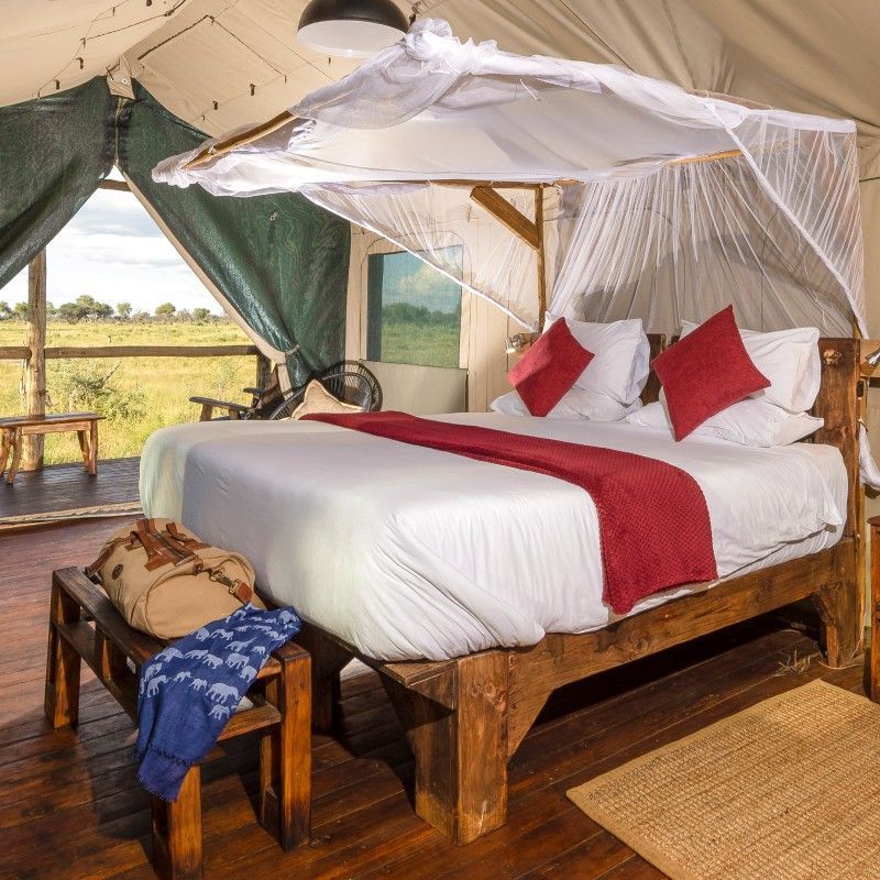 The bed inside one of the tents at Mogoelo Camp in Botswana is captured in this elegant travel photograph, showcasing a restful retreat set within a pristine wilderness environment. A well-appointed bed dressed in crisp linens and soft neutral tones forms the focal point of the tent, creating a sense of comfort and calm after a day on safari. Canvas walls, natural wood furnishings, and subtle decorative details reflect the camp’s understated design and close connection to nature. Openings allow gentle light and fresh air to filter through, enhancing the feeling of space and immersion in the surrounding landscape. The setting embodies the balance between authentic safari living and refined simplicity, offering guests a tranquil and memorable stay in one of Botswana’s remote and wildlife-rich regions. Inspiration Africa specializes in bespoke, tailor-made journeys to Botswana and across Africa, crafting unforgettable safari experiences in extraordinary wilderness destinations.
