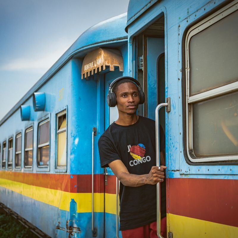 Experience a vibrant moment of everyday life in the Democratic Republic of Congo with this captivating photo of a young man wearing headphones aboard a train painted in the colors of the DRC flag. His relaxed posture and focused expression reflect a sense of personal rhythm amid the movement of the train, while the bold red, blue, and yellow carriages celebrate national pride. The dynamic scene captures the energy of Congolese culture and the pulse of daily travel through the country’s landscapes. Inspiration Africa designs tailor-made journeys that immerse you in authentic cultural experiences across Africa. Let us create your personalized adventure to explore the people, stories, and vibrant life of the DRC.