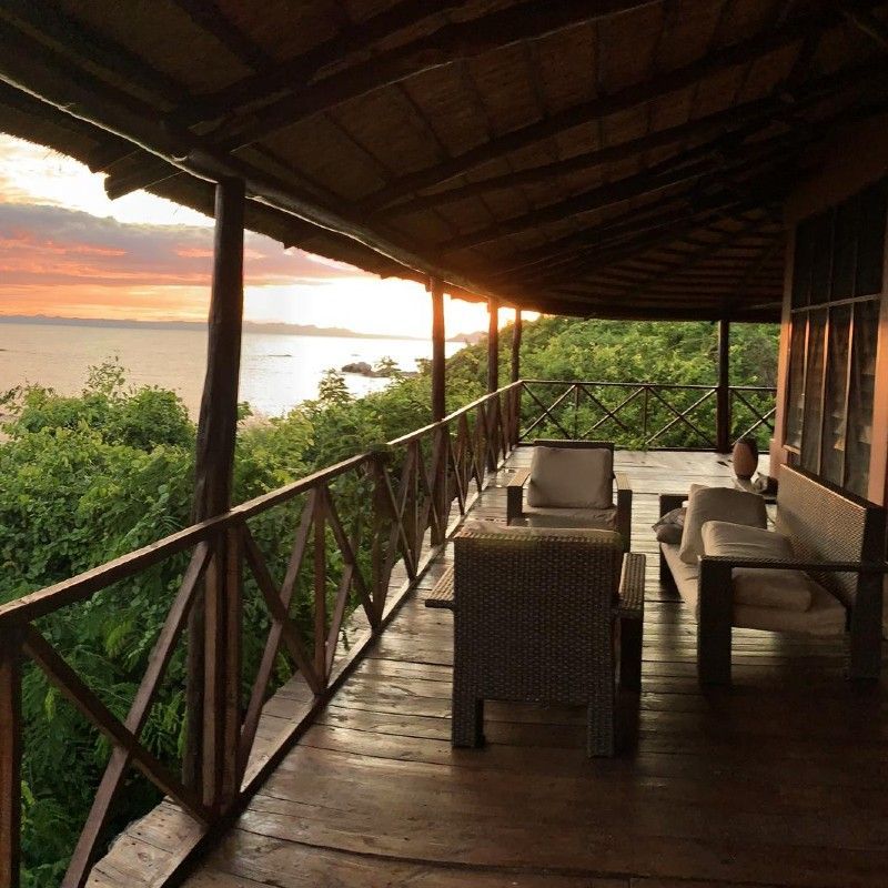 A veranda at Blue Zebra Island Lodge in Malawi overlooking a beautiful sunset across Lake Malawi is captured in this evocative travel photograph, highlighting a serene lakeside retreat. From the open balcony, uninterrupted views stretch across the calm water as the sky glows with warm shades of orange, pink, and gold. Soft evening light reflects on the lake’s surface, creating a tranquil and immersive atmosphere that emphasizes relaxation and connection with nature. Comfortable seating invites guests to pause and enjoy the peaceful surroundings. Inspiration Africa curates bespoke, tailor-made journeys to Malawi and across Africa, combining island escapes, wildlife encounters, and scenic experiences in extraordinary destinations.