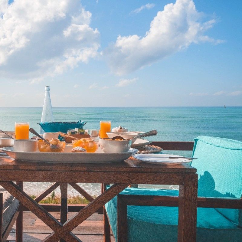 A guest enjoying breakfast by the sea at Coral Lodge in Mozambique is captured in this inviting travel photograph, highlighting a tranquil and scenic coastal experience. A table is set with fresh local dishes and beverages, while the turquoise waters of the Indian Ocean stretch to the horizon, framed by the lodge’s tropical surroundings. Soft morning light illuminates the scene, enhancing the vibrant colors and serene atmosphere, creating a sense of relaxation and connection with nature. The image reflects the lodge’s focus on comfort, immersive coastal views, and memorable dining experiences. Inspiration Africa curates bespoke, tailor-made journeys to Mozambique and across Africa, combining luxury beach stays with immersive coastal and wildlife experiences.
