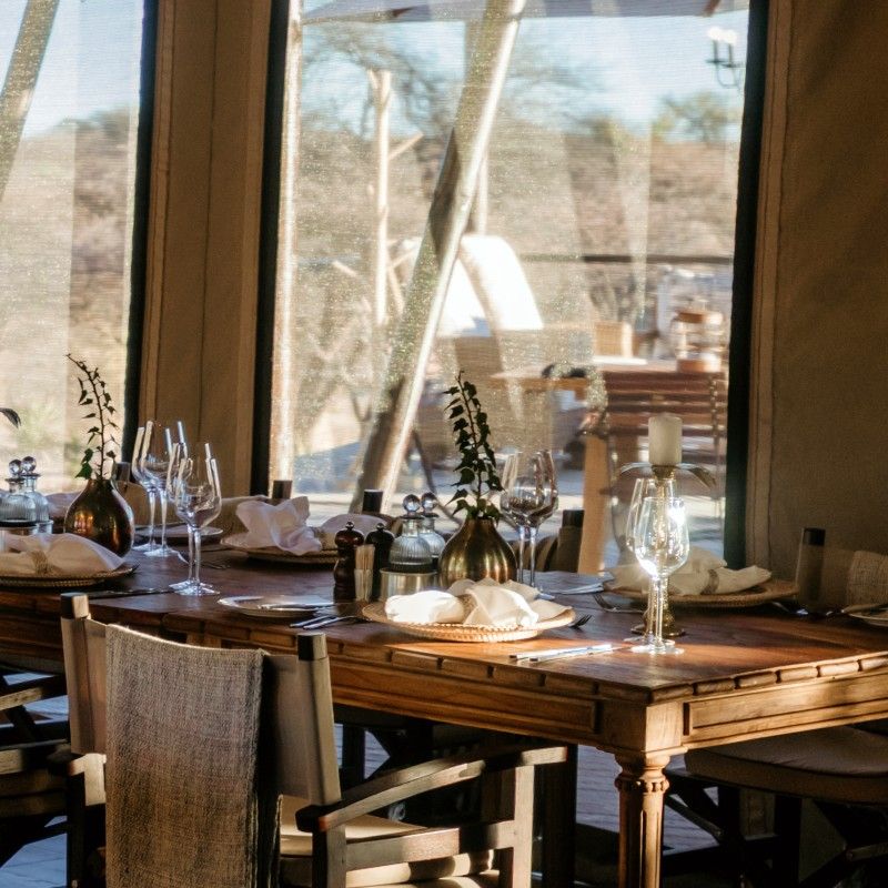 The dining room at Otijwa Thornbush Tented Camp in Namibia is captured in this inviting travel photograph, showcasing a warm and elegant space designed for comfort and connection with the surrounding wilderness. Natural materials, earthy tones, and rustic yet refined décor create a stylish yet relaxed atmosphere, while large windows and open areas bring in natural light and panoramic views of the savannah. The setting provides an intimate and welcoming environment for meals after a day of safari exploration, perfectly blending luxury with authentic bush camp charm. Ideal for safari enthusiasts, photographers, and travelers seeking immersive experiences, this scene captures the elegance, tranquility, and intimate atmosphere that define Otijwa Thornbush Tented Camp. Inspiration Africa specializes in bespoke, tailor-made journeys to Namibia and across Africa, crafting unforgettable lodge stays and extraordinary safari experiences in exceptional landscapes.