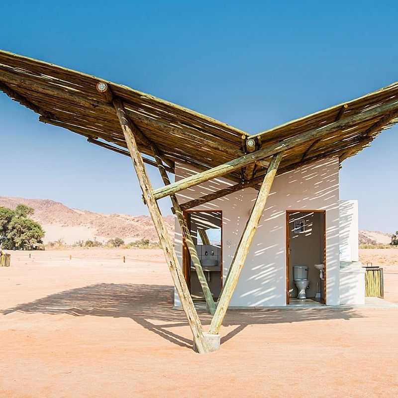 The unique exterior of Sesriem Oshana Campsite in Namibia is captured in this striking travel photograph, highlighting its distinctive design set against the dramatic desert landscape of the Namib. Rustic yet functional structures blend seamlessly with the surrounding environment, using natural materials and earthy tones that echo the hues of the dunes and open plains. Open spaces and thoughtfully arranged tents or shelters create a welcoming and authentic bush camping experience, allowing guests to feel fully immersed in the stark beauty of the Namib Desert. Ideal for adventure travelers, photographers, and nature enthusiasts, this scene captures the harmony of simple design, rugged wilderness, and the unforgettable atmosphere that defines Sesriem Oshana Campsite. Inspiration Africa specializes in bespoke, tailor-made journeys to Namibia and across Africa, crafting immersive desert camping experiences and extraordinary wilderness adventures.