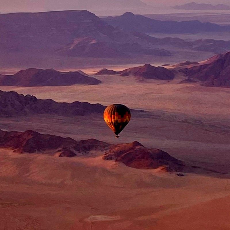 Aerial view of a hot air balloon drifting silently over the vast desert landscapes of Namibia at sunrise, where golden light washes across towering red sand dunes and endless horizons. The soft morning glow creates dramatic contrasts of shadow and color across the ancient Namib Desert, one of Africa’s most iconic and otherworldly environments. From above, the balloon floats peacefully through the still morning air, offering a breathtaking perspective of rolling dunes, shifting textures, and the untouched beauty of this remote wilderness.
Inspiration Africa specializes in bespoke, tailor-made journeys across Namibia and the African continent, creating immersive travel experiences that combine extraordinary landscapes, luxury adventure, and authentic cultural discovery. From scenic hot air balloon safaris over the Namib Desert to unforgettable safari experiences, every itinerary is carefully curated to showcase the beauty, diversity, and spirit of Africa.
