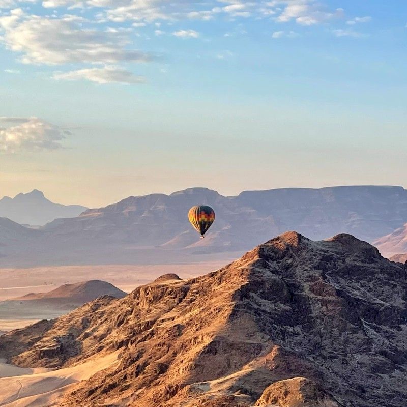 Gaze upon a breathtaking balloon flight drifting silently over Namibia’s Namib Desert, captured in this striking aerial photograph. Hot air balloons float above vast seas of rolling sand dunes, glowing in soft morning light and revealing the scale and timeless beauty of one of the world’s oldest deserts. From above, the patterns, colors, and endless horizons of the Namib create a truly surreal landscape. Experiencing the desert by balloon offers a peaceful and unforgettable perspective on Namibia’s raw wilderness. Inspiration Africa specializes in designing bespoke, tailor-made journeys that showcase Africa’s most extraordinary landscapes and once-in-a-lifetime travel experiences.