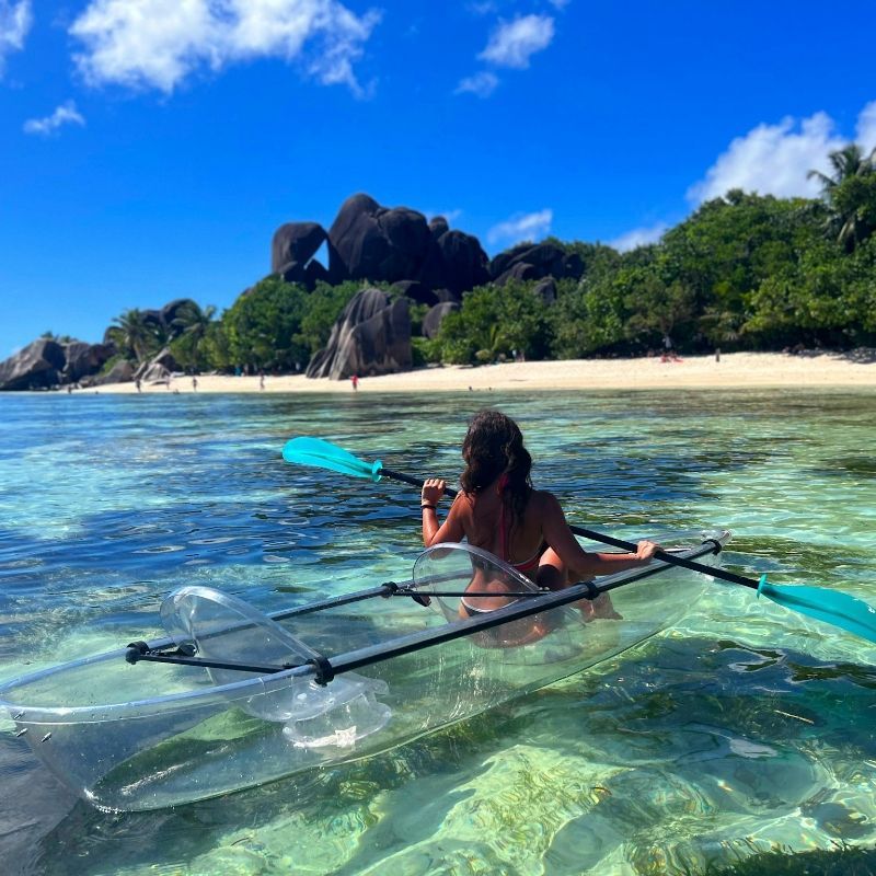 A tourist paddles a transparent kayak through the stunning turquoise waters surrounding La Digue, Seychelles, captured in this vibrant adventure travel photograph. Surrounded by pristine beaches, granite boulders, and crystal-clear waters, kayaking here offers an immersive way to explore one of the world’s most beautiful island destinations. Paddlers can admire colorful marine life beneath the kayak, navigate calm lagoons, and experience Seychelles’ serene tropical scenery up close. Ideal for nature lovers and adventure travelers, this activity showcases the islands’ unspoiled landscapes and idyllic ocean vistas. Inspiration Africa specializes in bespoke, tailor-made journeys to the Seychelles and across Africa, creating authentic, unforgettable travel experiences that combine adventure, natural beauty, and exclusive destinations.