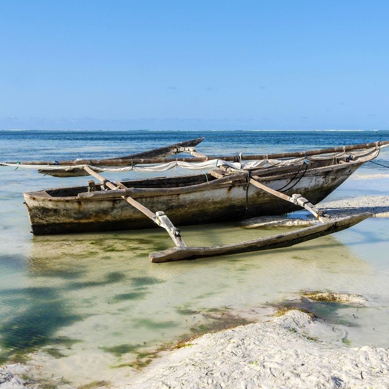 A wooden boat is floating on top of a sandy beach in the ocean.