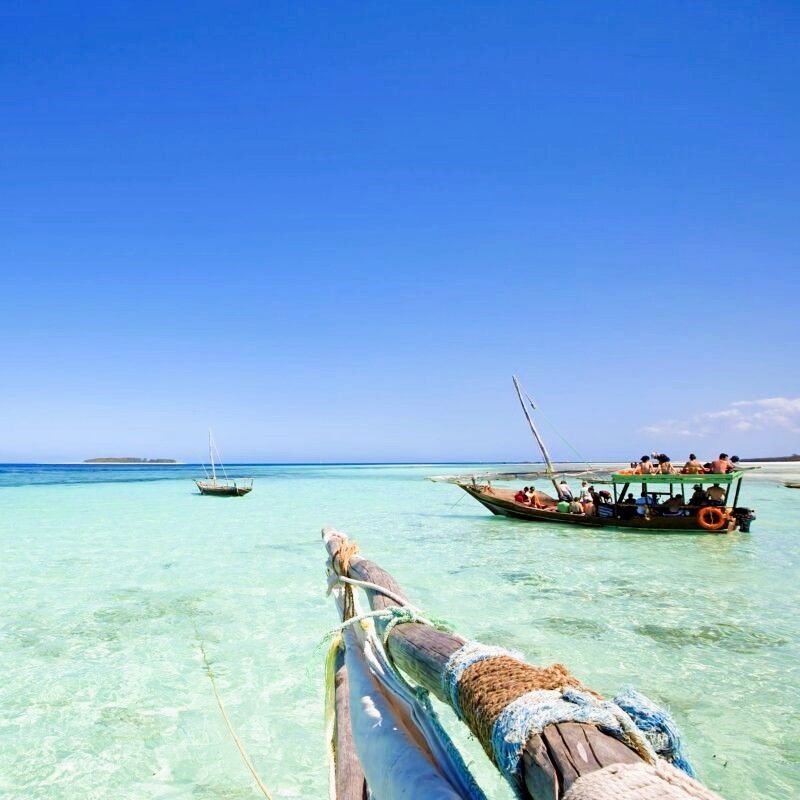 The crystal-clear turquoise waters of Zanzibar frame the bow of a traditional wooden dhow in this captivating travel photograph. Gently floating on the Indian Ocean, the iconic sailing vessel reflects the island’s rich Swahili heritage and centuries-old maritime traditions. Beneath the calm, transparent waters, coral reefs and shifting sands create a vivid palette of blues and greens, highlighting Zanzibar’s reputation as one of Africa’s most beautiful island destinations. Ideal for beach lovers, cultural explorers, and photographers, this scene captures the timeless rhythm of coastal life. Inspiration Africa specializes in bespoke, tailor-made journeys to Zanzibar and across Africa, crafting authentic island experiences that combine culture, relaxation, and unforgettable ocean adventures.