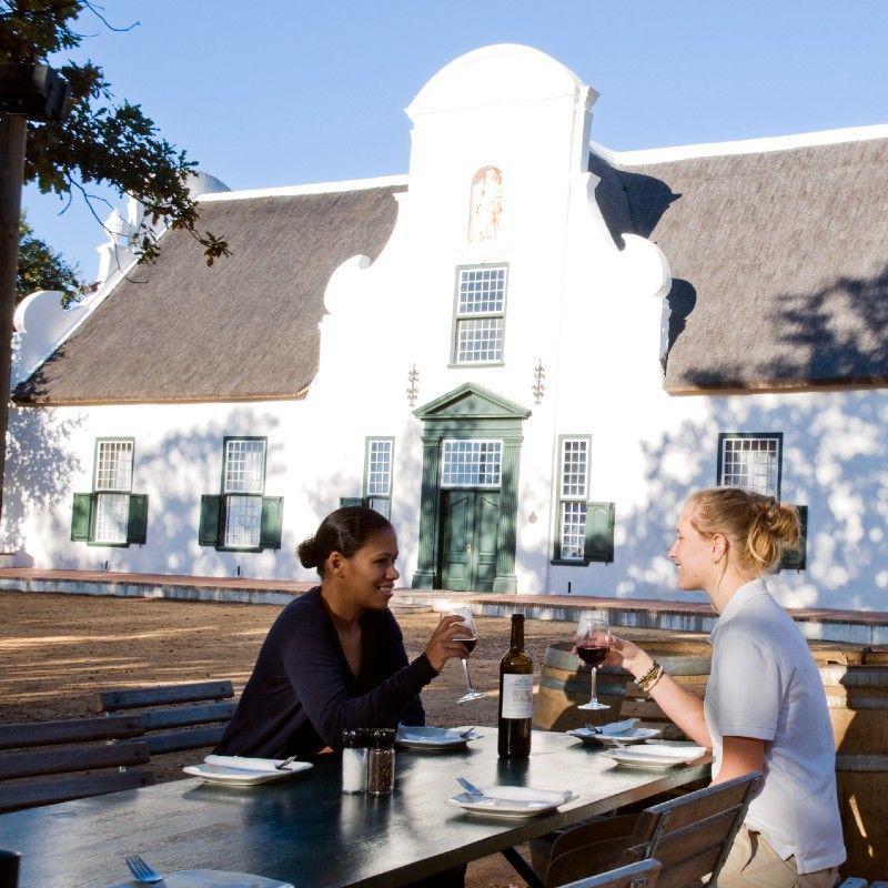 Couple wine tasting on the porch of a traditional Cape Dutch farm in Franschhoek, South Africa—a refined culinary experience curated by Inspiration Africa.