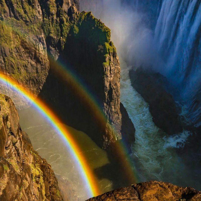 Gaze upon the breathtaking beauty of Victoria Falls from the Zambian side, captured with a vivid rainbow arcing through the mist. This striking photograph showcases the immense power and scale of the falls as sunlight illuminates the cascading water, creating a dazzling spectrum of colors. Known locally as Mosi-oa-Tunya, “the Smoke That Thunders,” Victoria Falls is one of Africa’s most iconic natural wonders and a UNESCO World Heritage Site. Witnessing a rainbow at the falls is a magical and unforgettable experience. Inspiration Africa specializes in designing bespoke, tailor-made journeys that combine iconic landscapes with extraordinary travel experiences across Africa’s most remarkable destinations.