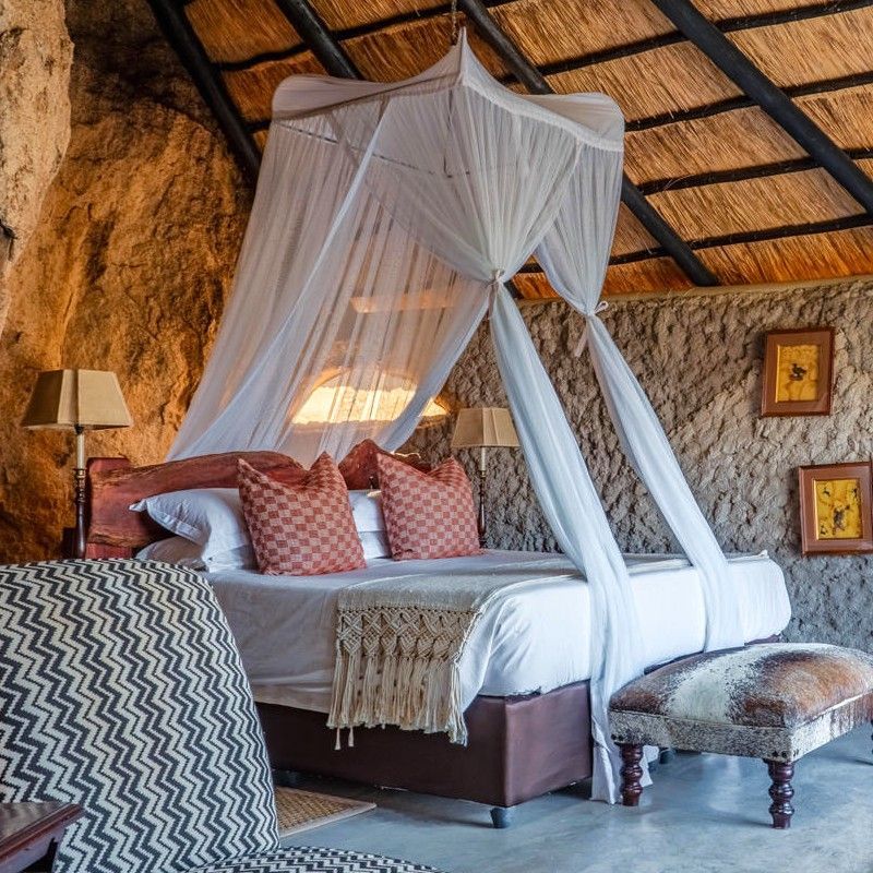 The interior of a standard room at Amalinda Lodge in Zimbabwe is featured in this atmospheric travel photograph, showcasing a thoughtfully designed space built around natural granite boulders. A comfortable bed, handcrafted furnishings, and stone elements create a warm and earthy ambiance that reflects the lodge’s unique character and connection to its surroundings. Soft lighting and natural textures enhance the sense of calm and privacy, while open design features allow the room to blend seamlessly with the landscape outside. The interior balances understated luxury with authenticity, offering guests a peaceful retreat immersed in the timeless beauty of Matobo Hills. Inspiration Africa specializes in bespoke, tailor-made journeys to Zimbabwe and across Africa, crafting unforgettable travel and safari experiences in extraordinary destinations.