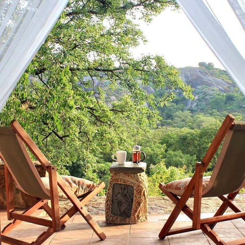 The balcony at Big Cave Camp in Zimbabwe is captured in this serene travel photograph, overlooking the vast wilderness of the Matobo Hills. From the elevated vantage point, guests can take in sweeping views of rocky outcrops, rolling hills, and scattered trees, where wildlife such as antelope and birds often move freely. Natural materials and simple design create a seamless connection between the camp and its surroundings, offering a tranquil space to relax and immerse in the landscape. Soft light and open space enhance the sense of calm and perspective, reflecting the authentic safari experience of observing Zimbabwe’s extraordinary scenery. Inspiration Africa specializes in bespoke, tailor-made journeys to Zimbabwe and across Africa, crafting unforgettable safari experiences in extraordinary wilderness destinations.