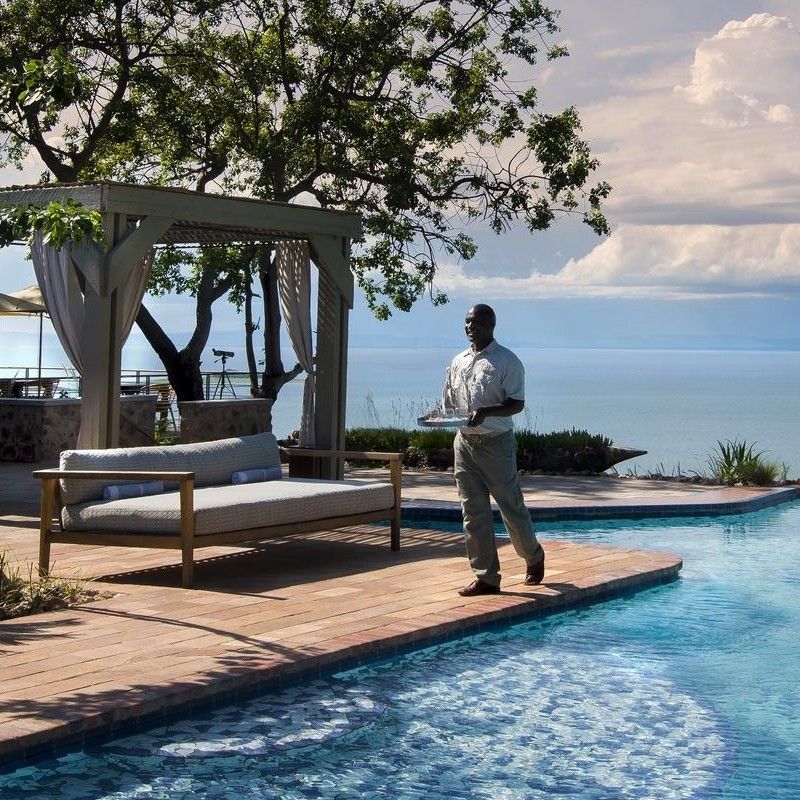 The swimming pool at Bumi Hills Safari Lodge in Zimbabwe is captured in this breathtaking travel photograph, set on the edge of the escarpment overlooking Lake Kariba. The infinity-style pool reflects the deep blue of the lake and the warm hues of the sky, creating a seamless visual connection between water and horizon. Comfortable sun loungers and shaded areas provide spaces for relaxation, while the surrounding natural vegetation enhances the sense of privacy and immersion in the landscape. The scene conveys serenity, understated luxury, and spectacular views, highlighting Bumi Hills Safari Lodge as an exclusive retreat where guests can unwind while taking in one of Zimbabwe’s most iconic vistas. Inspiration Africa specializes in bespoke, tailor-made journeys to Zimbabwe and across Africa, crafting unforgettable travel experiences in extraordinary destinations.