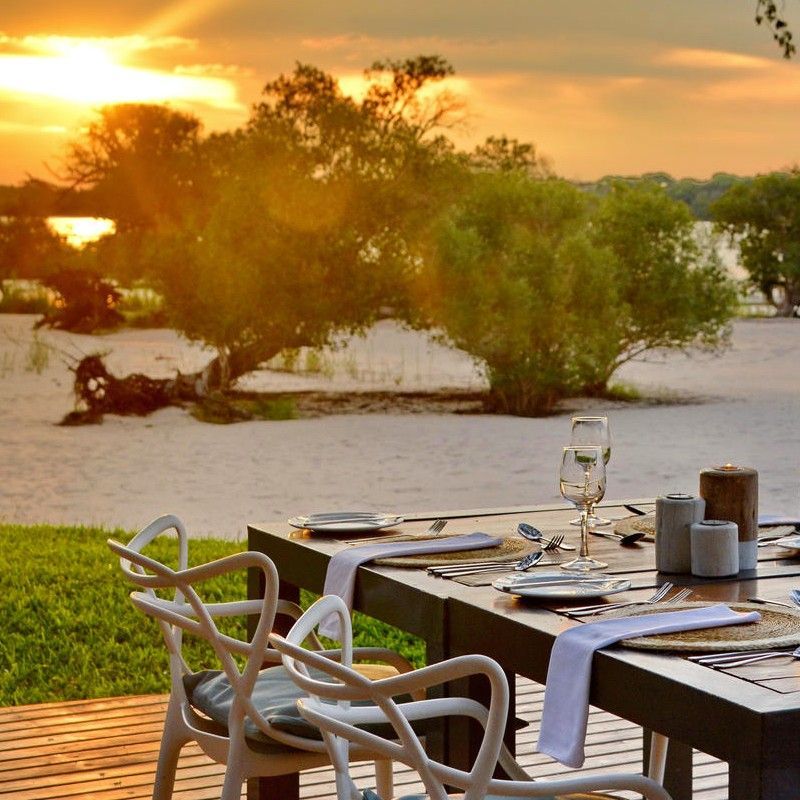 Dining outdoors next to the Zambezi River at Chundu Island in Zimbabwe is captured in this inviting travel photograph, showcasing a serene and scenic setting for enjoying meals. Tables are arranged along the riverbank, surrounded by lush vegetation and open skies, allowing guests to take in sweeping views of the water and wildlife that often appears along the river’s edge. Natural materials and elegant, understated design create a harmonious connection with the environment, emphasizing tranquility and immersion in nature. The scene conveys the essence of an authentic Zambian safari experience, combining relaxed outdoor dining, stunning riverside scenery, and unforgettable encounters with Zimbabwe’s remarkable wildlife. Inspiration Africa specializes in bespoke, tailor-made journeys to Zimbabwe and across Africa, crafting extraordinary safari experiences in remarkable wilderness destinations.