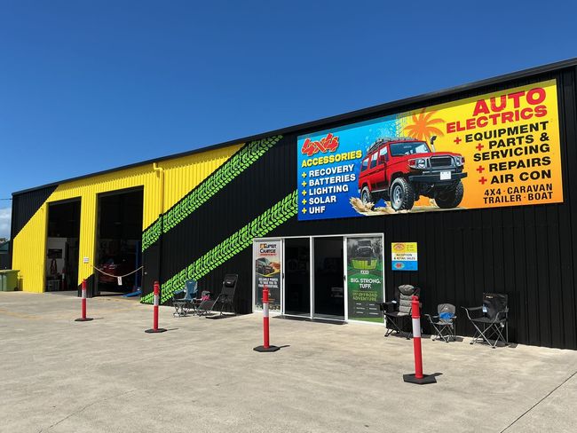 Auto Electrician shop with yellow and black exterior, large sign featuring a red truck, open garage bays.
