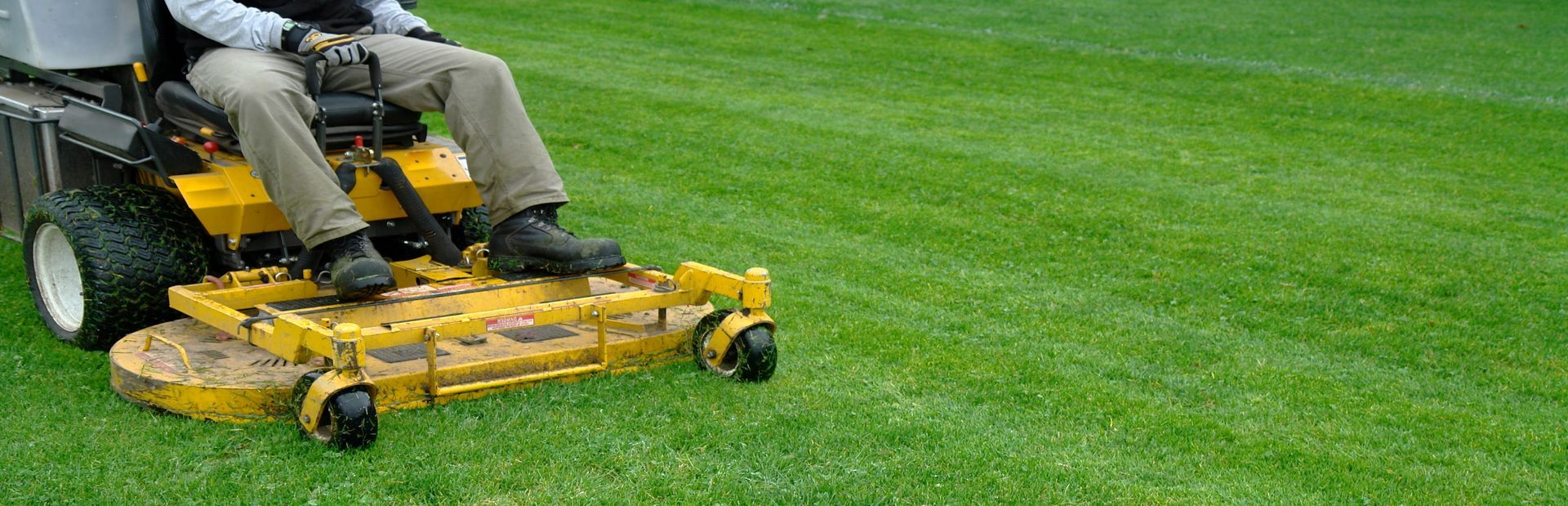 A person on a yellow riding lawnmower cutting green grass in a field.
