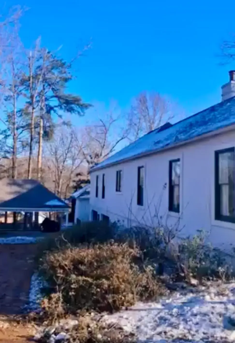 Snowy yard beside a white house under a bright blue sky