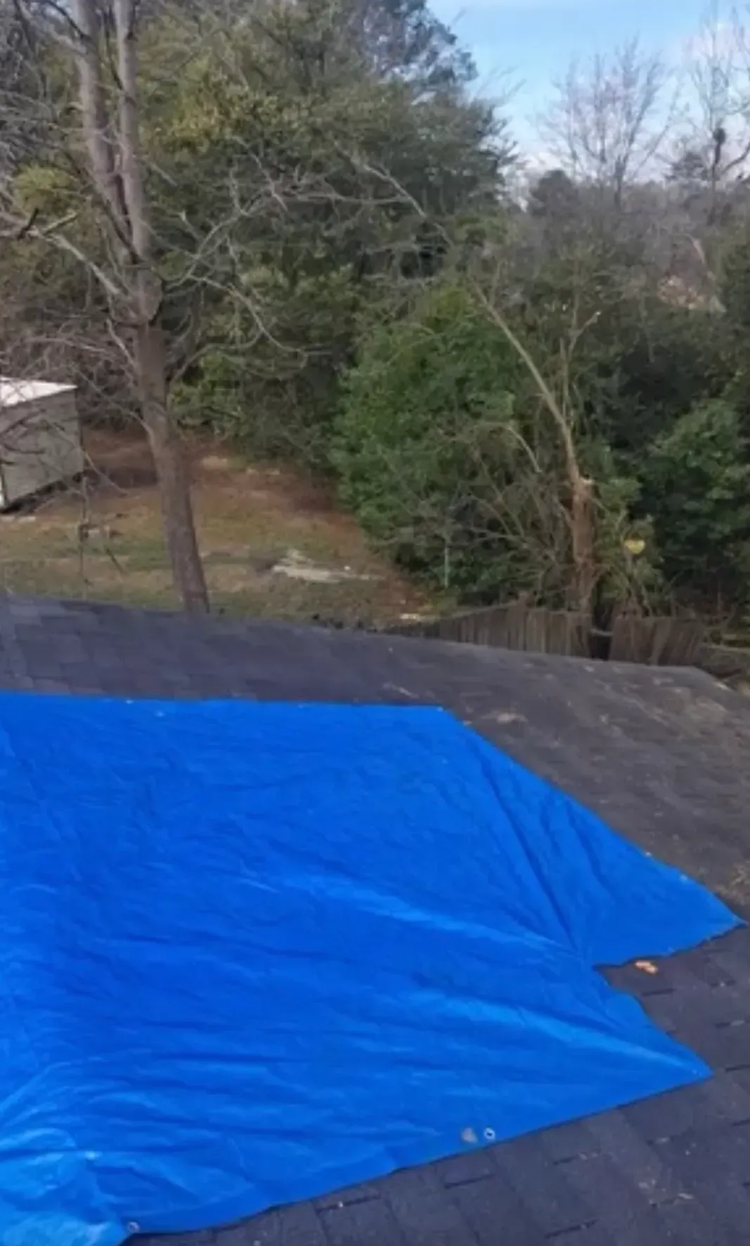 Blue tarp covering a rooftop, with trees and a yard in the background.