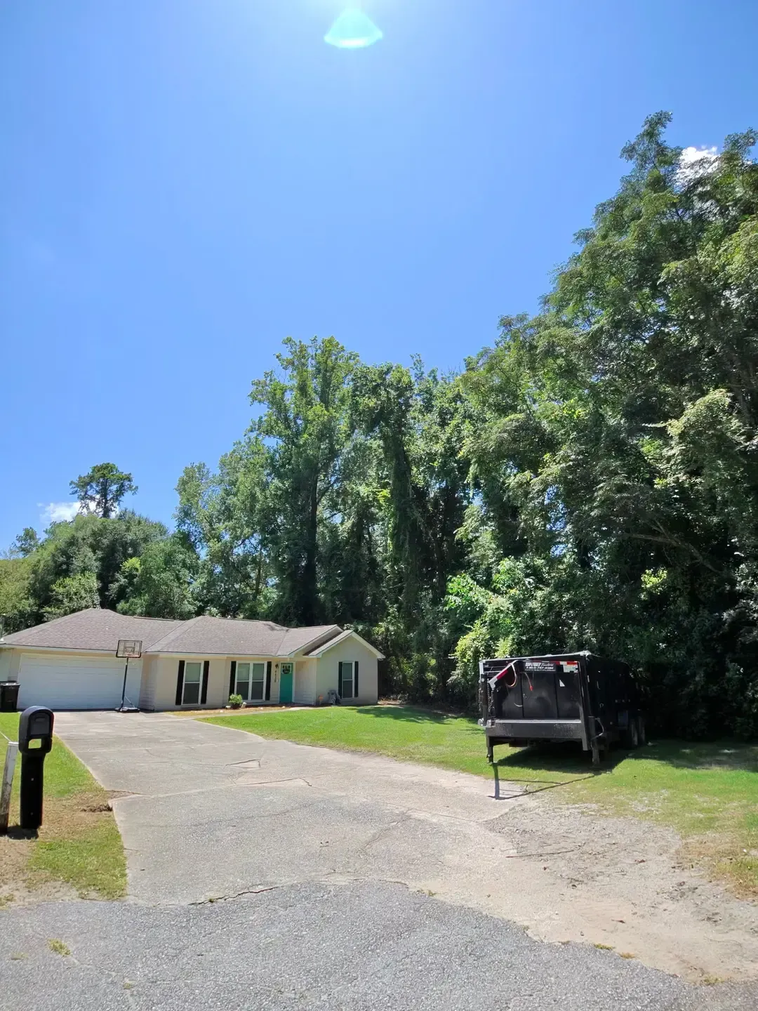 Driveway leading to a small white house with trees under a bright blue sky
