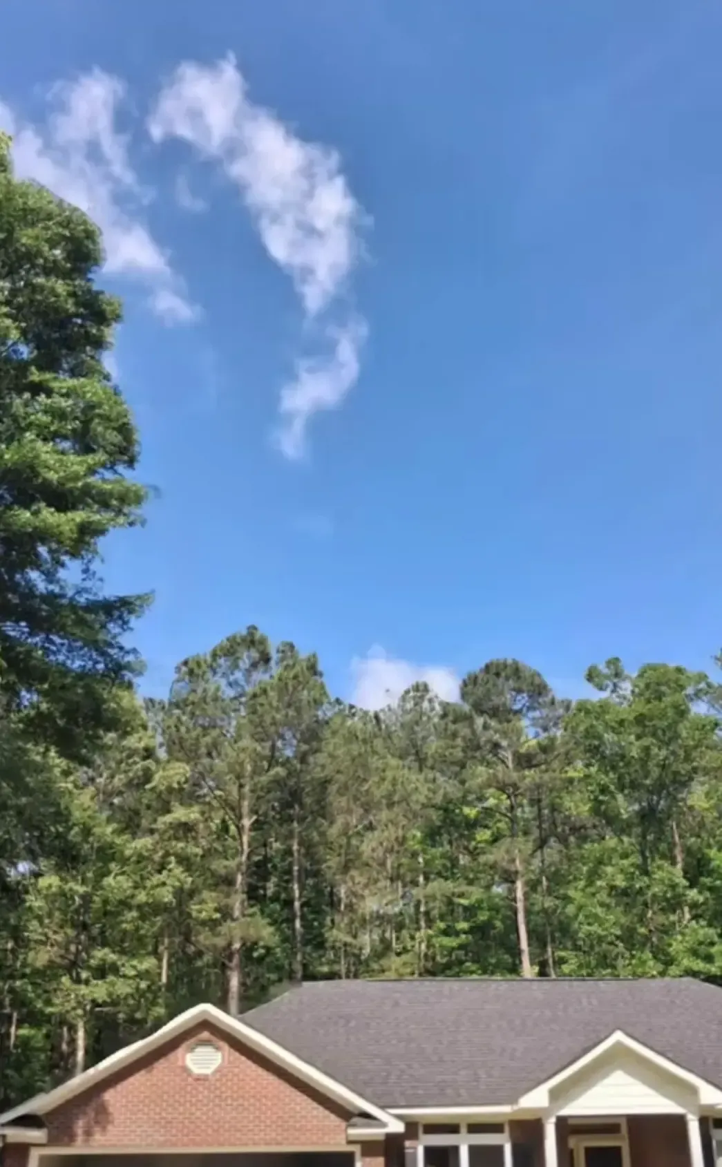 Blue sky with a few clouds above tall trees and rooftops of suburban houses