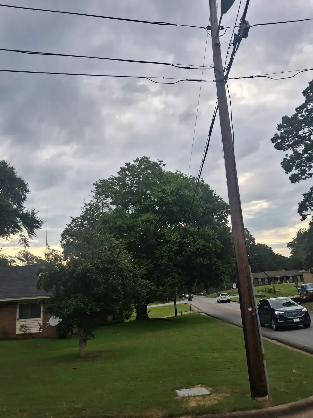 Suburban street with utility pole, trees, cloudy sky, and parked cars beside houses