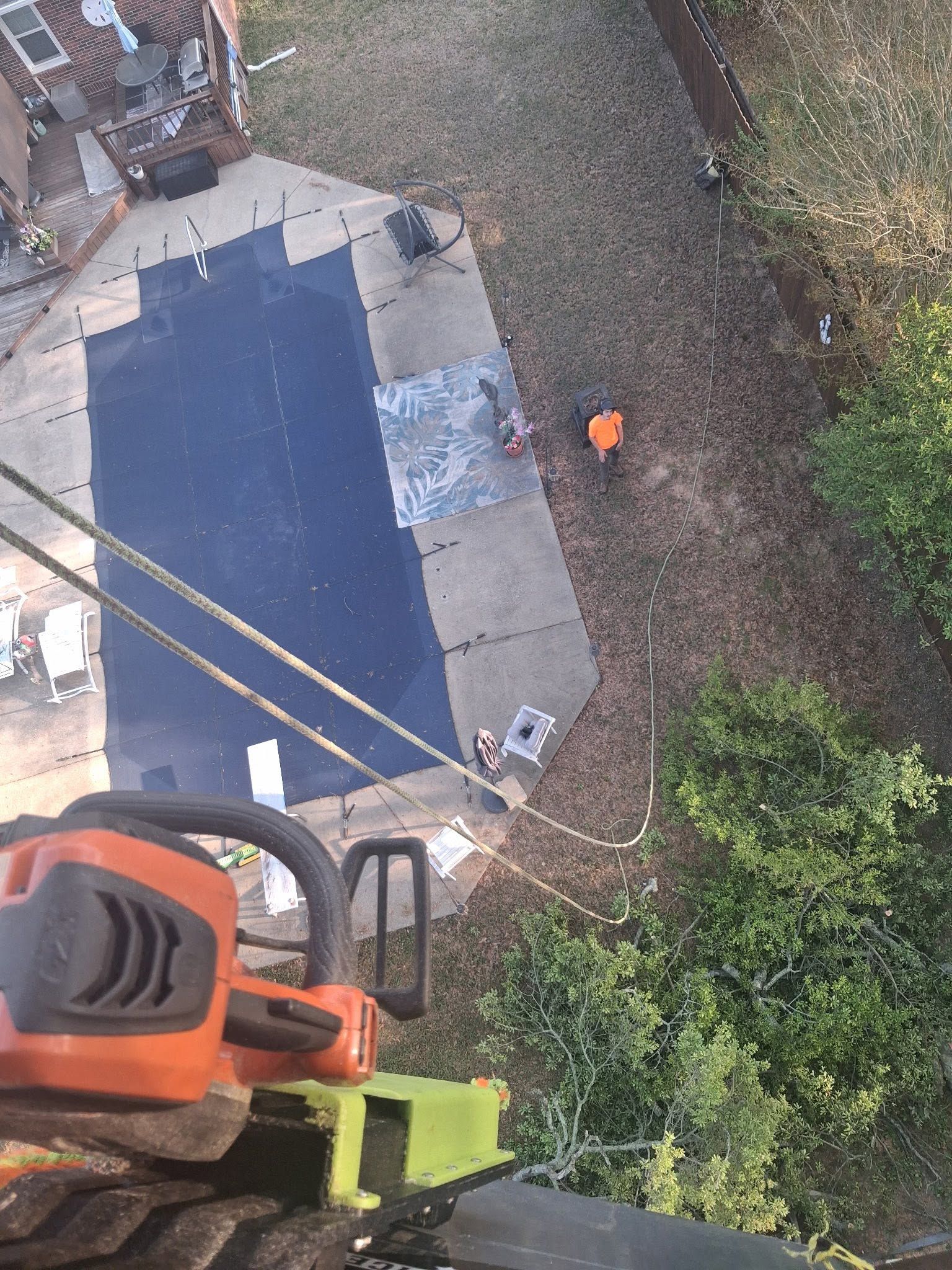 Aerial view of a blue-roofed building and yard, with a worker in orange near the right side.