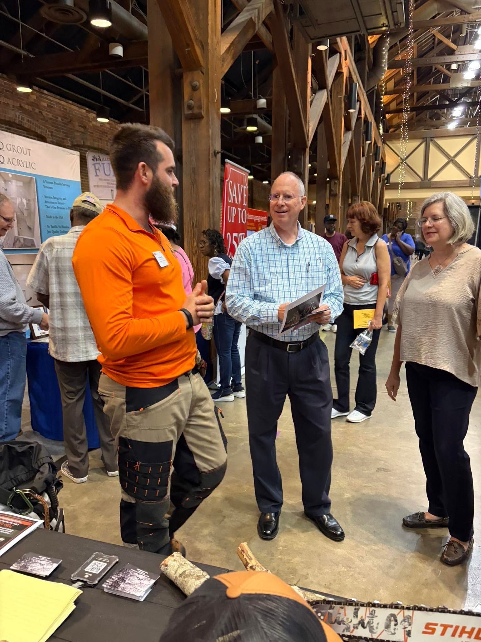 Three people chatting at a trade show booth in a wooden indoor venue.