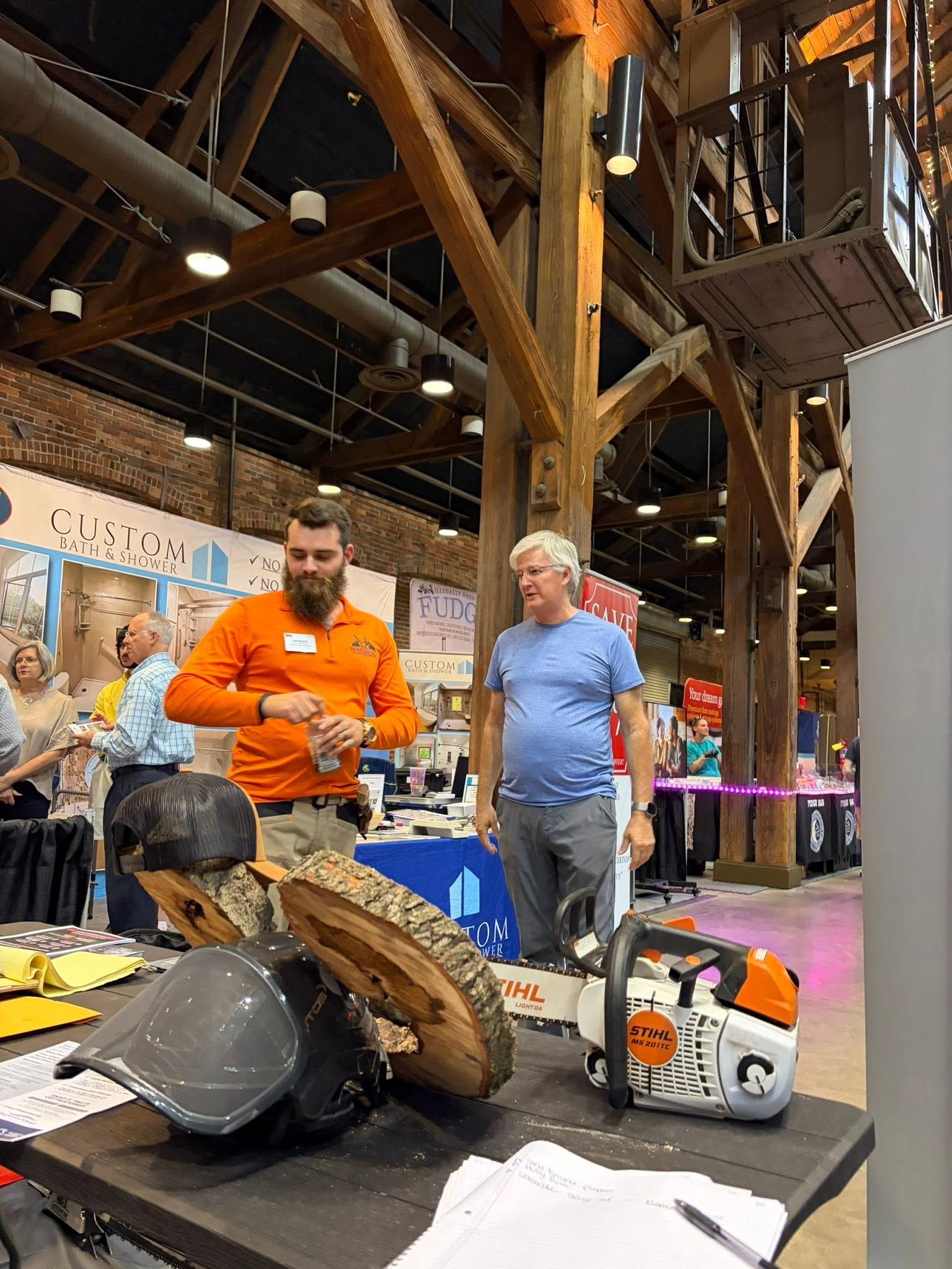 People standing by a table with tools and equipment in a large indoor expo hall.