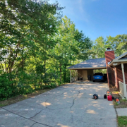 Driveway beside a brick house and garage, bordered by trees under a blue sky.