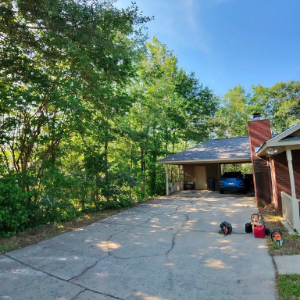 Driveway beside a brick house and garage, bordered by trees under a blue sky.