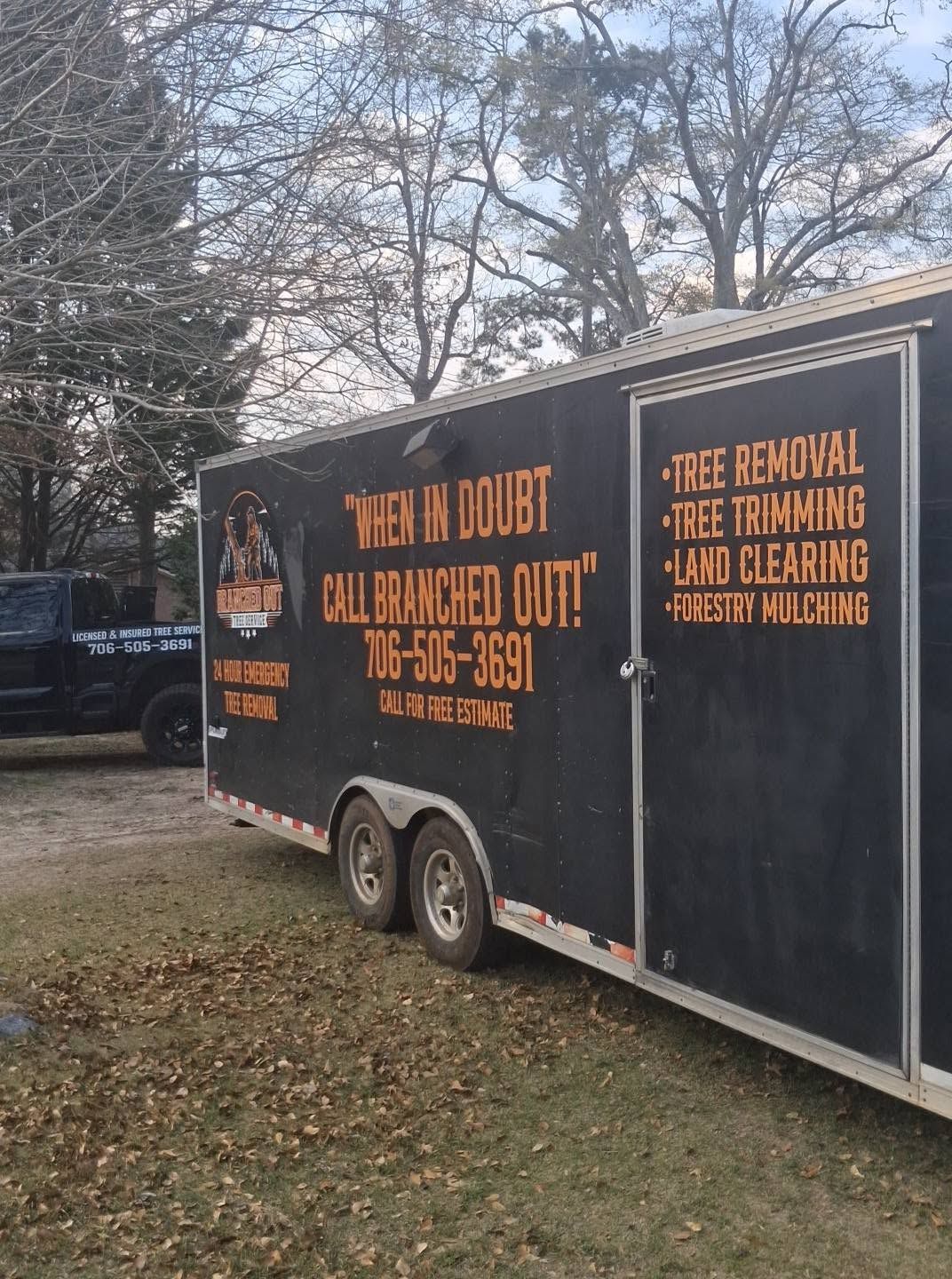 Black service trailer with orange text parked on grass near trees and a house at dusk