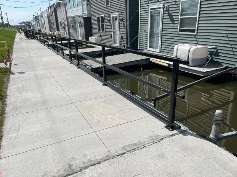 Concrete walkway beside house with black railing along a canal or water channel
