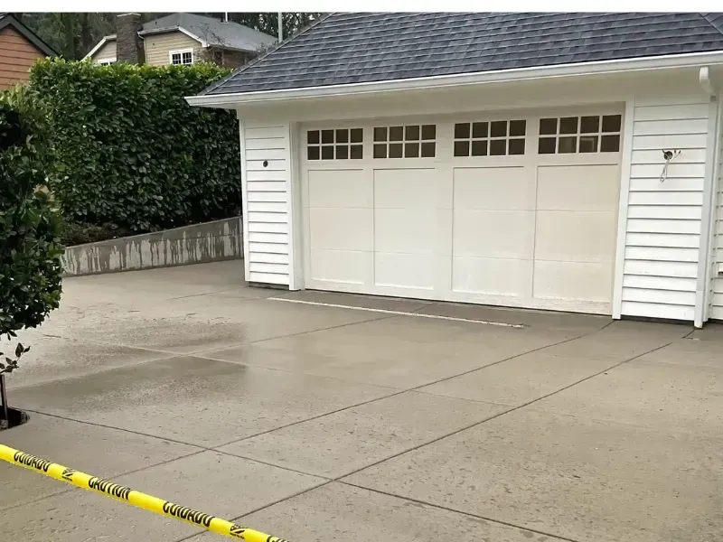 White garage with closed door on a gray concrete driveway. Yellow caution tape across the bottom left.