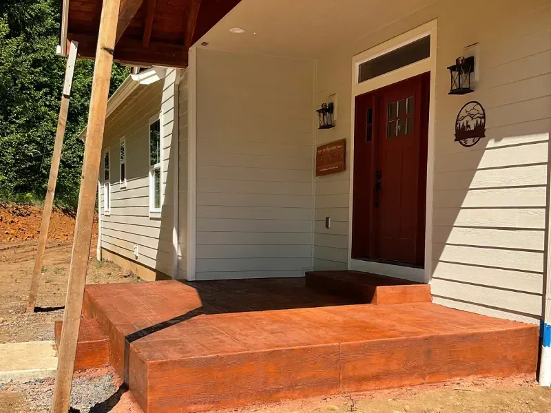 Front porch with red-brown concrete steps and a brown wooden door, light gray siding.